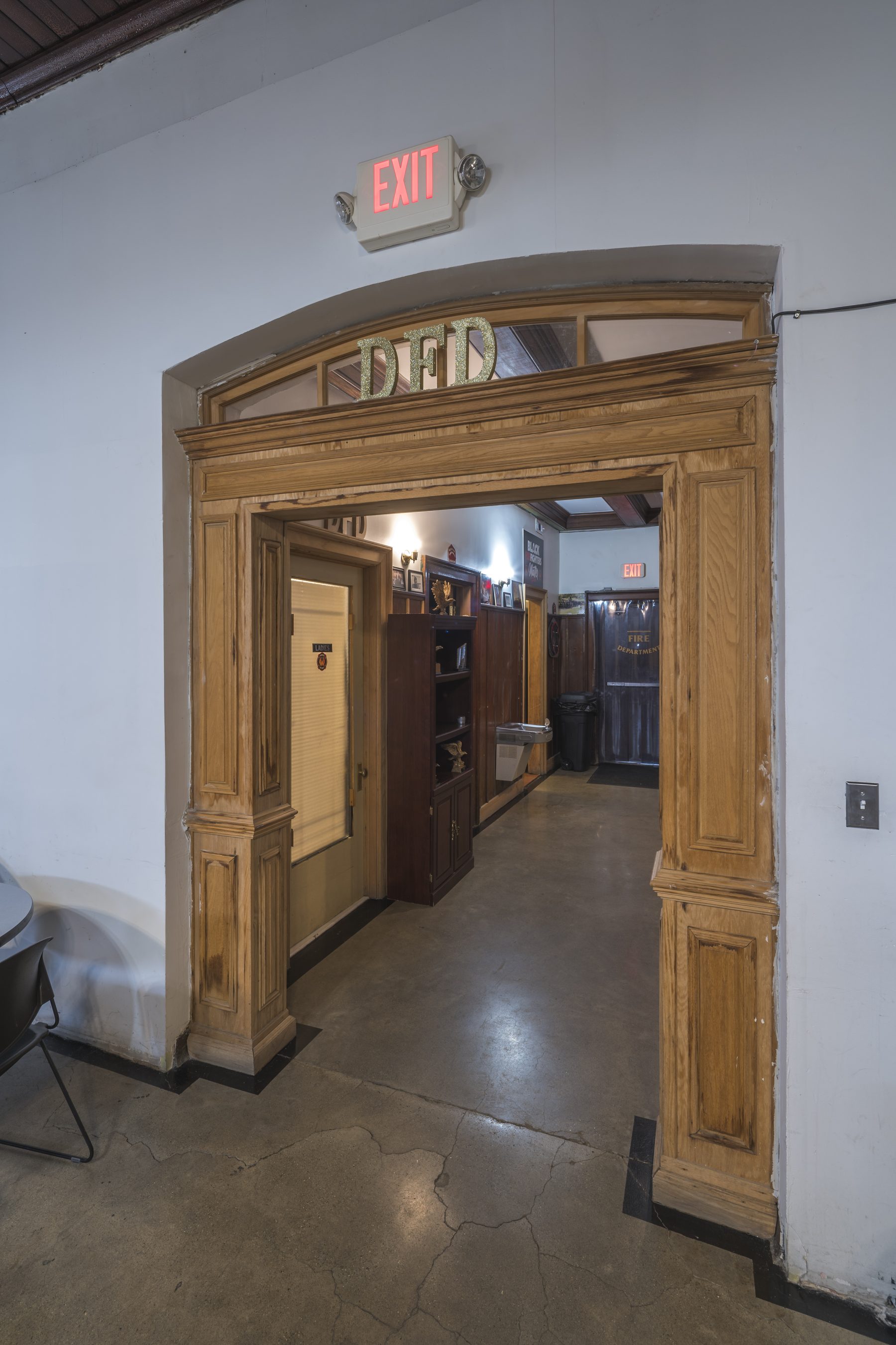 Ornate wooden archway inside Historic Engine 11 with DFD lettering above the doorway — the corridor leading from the foyer into the firehouse interior.