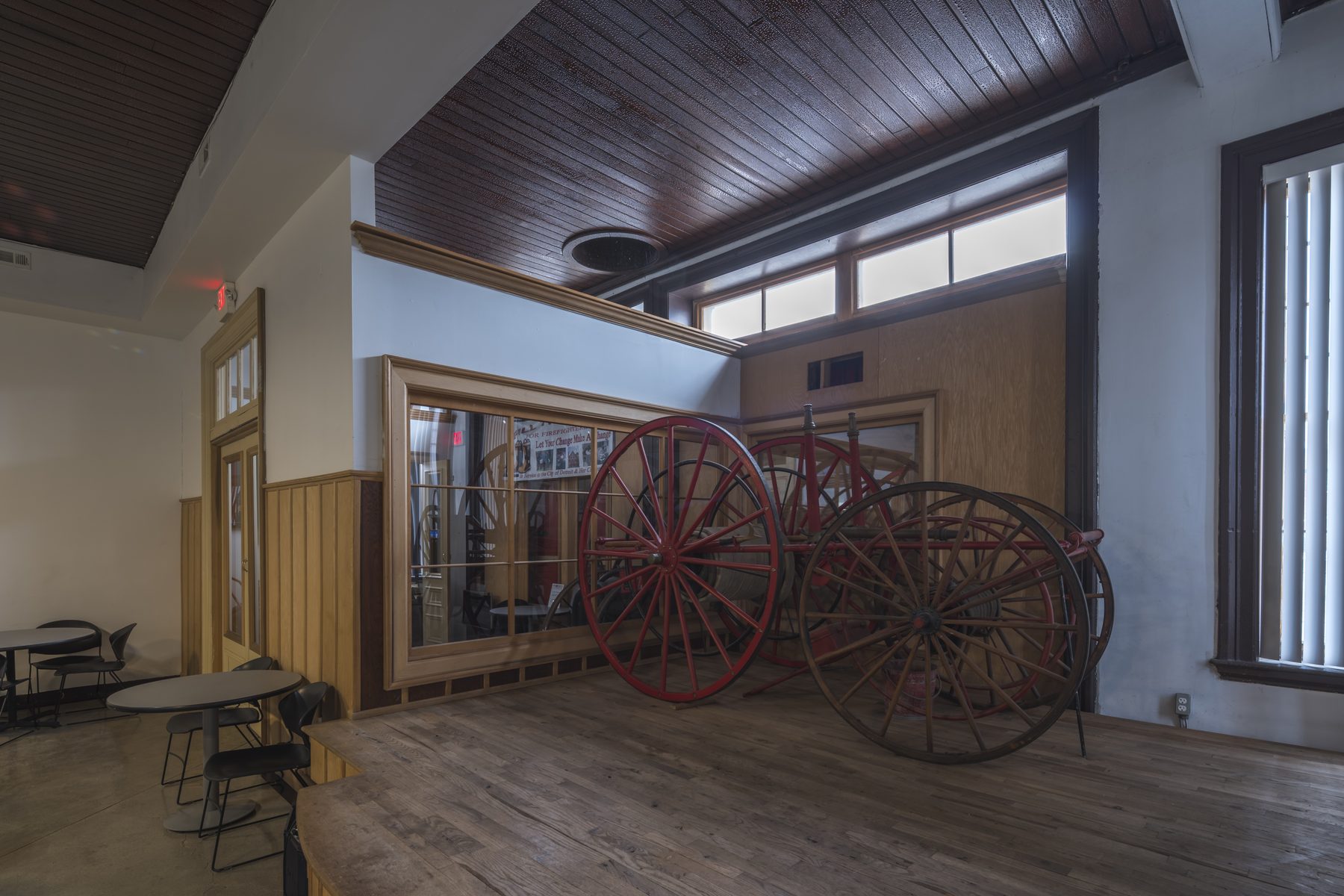 Historic Engine 11 banquet hall set for an event — antique fire hose reels displayed on the raised wood platform under a coffered wooden ceiling.