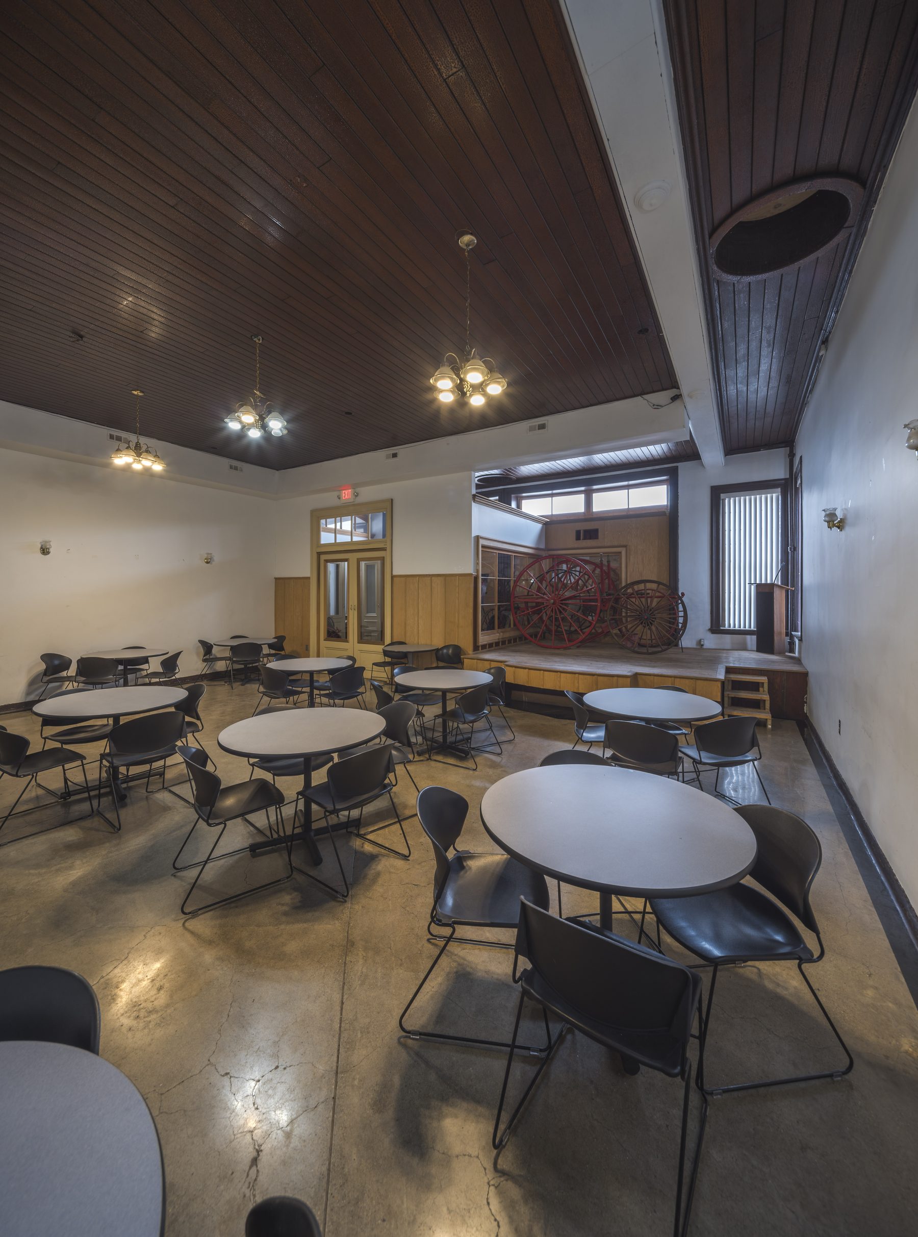 Wide view of the Historic Engine 11 banquet hall — round tables, stage with podium, and historic Detroit fire apparatus wheels on display.