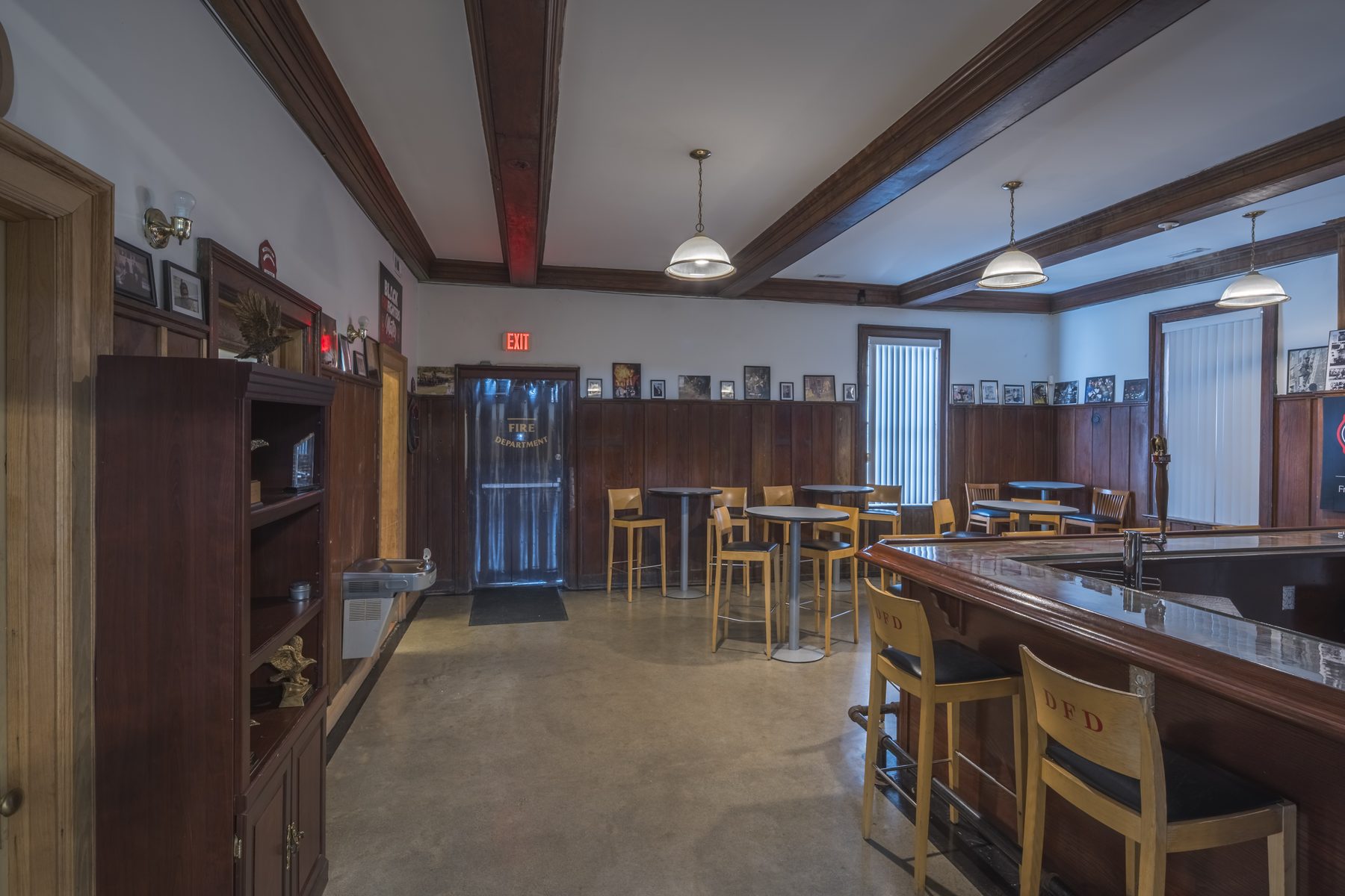 The bar and lounge at Historic Engine 11 — polished wood bar, DFD-branded stools, Phoenix Detroit memorabilia, and the Fire Department doorway curtain.