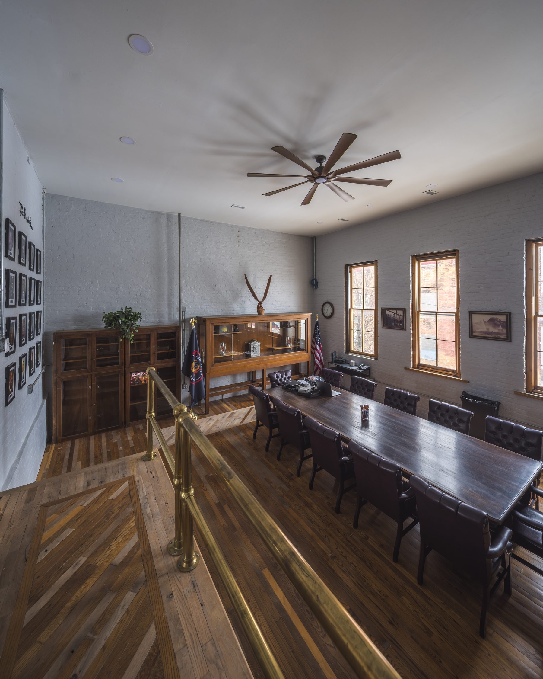 The upstairs meeting room at Historic Engine 11 — exposed brick walls, long dark wood conference table with leather chairs, parquet staircase with brass rails.