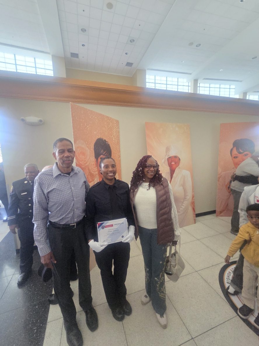 A Project 100 candidate at her Detroit Fire Department academy graduation, holding her certificate with family.