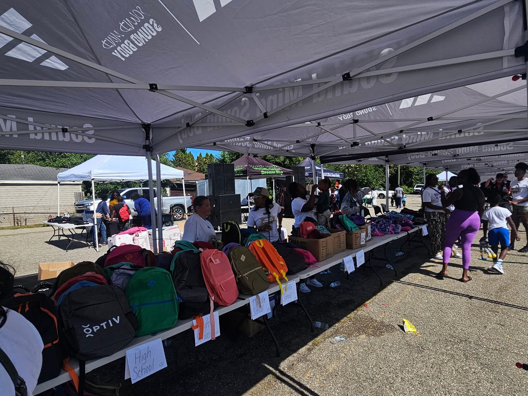 Phoenix backpack giveaway under event tents — rows of color-coded backpacks for Detroit students.
